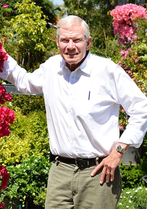 A man in a white shirt standing in front of a flower garden.
