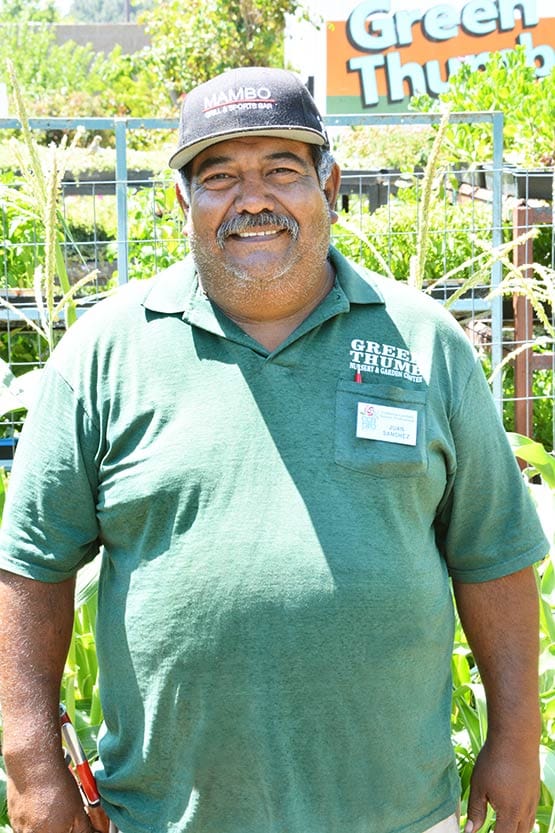 A man in a green shirt standing in front of a garden.