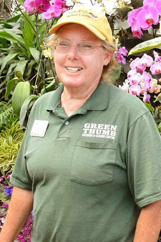 A woman in a green shirt standing in front of orchids.