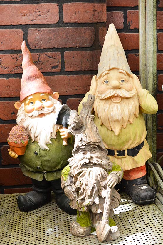 A group of gnome statues on a brick wall.