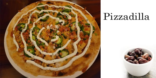 A pizza on a plate next to a cup of olives at the best garden center near me.