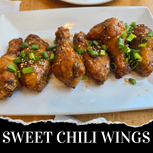 A rectangular plate of sweet chili chicken wings garnished with chopped green onions and sesame seeds, displayed on a wooden table. Text at the bottom reads "SWEET CHILI WINGS.