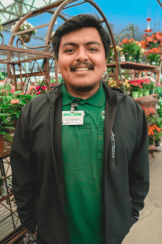 A man in a green jacket standing near a plant nursery.