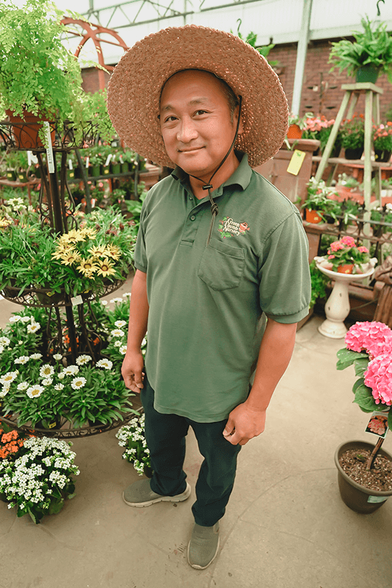 A man in a hat standing near a plant nursery.
