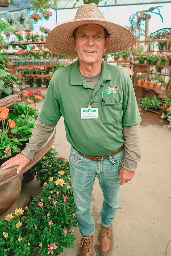 The man in the hat is standing in front of plants at the best plant nursery near me.
