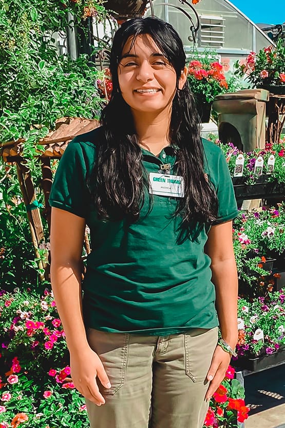 A woman in a green shirt standing in front of plants at the best plant nursery near me.