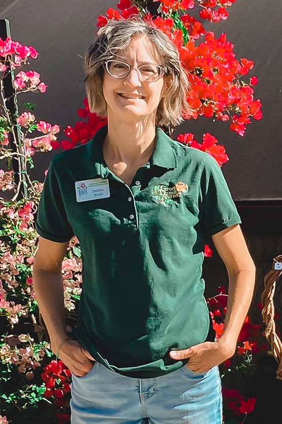 A woman in a green polo standing in front of flowers at the best plant nursery near me.