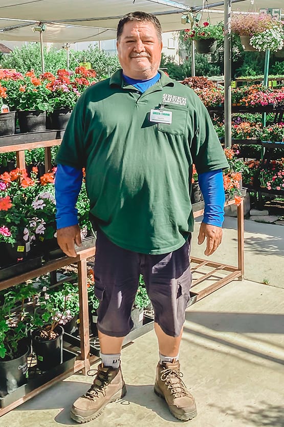 A man in a green shirt standing in front of potted plants at the nursery near me.