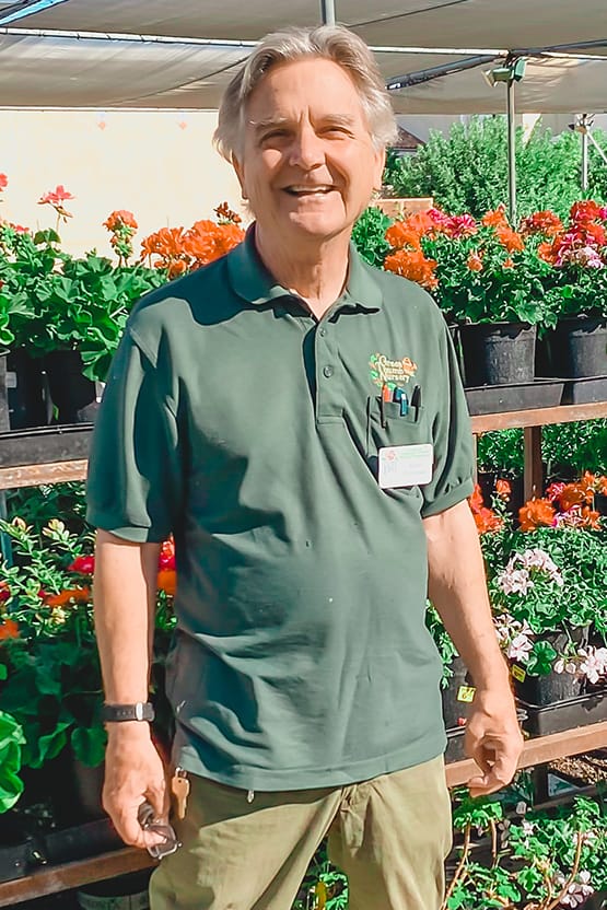 A man in a green shirt standing in front of potted plants at the best garden center near me.
