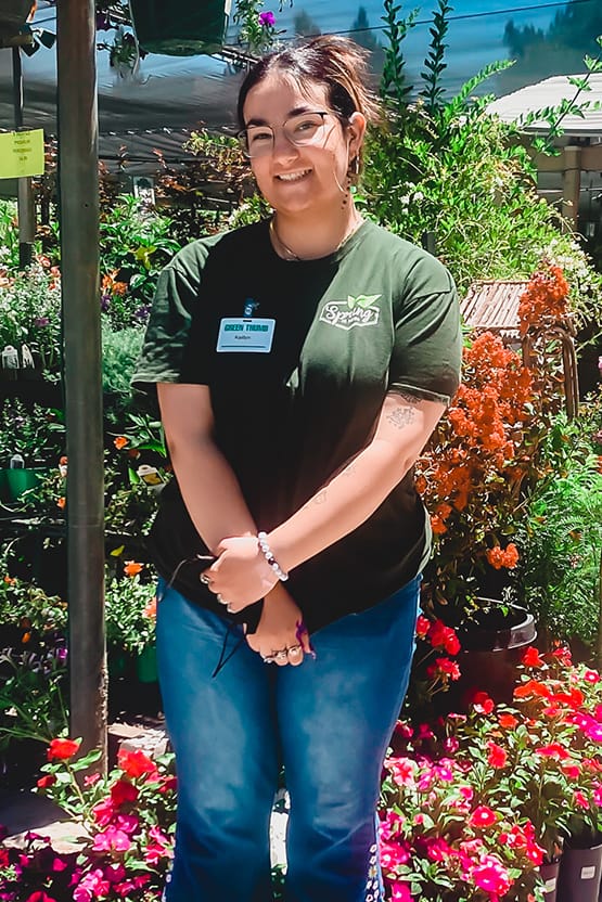 A woman standing in front of a flower garden at a garden center near me.