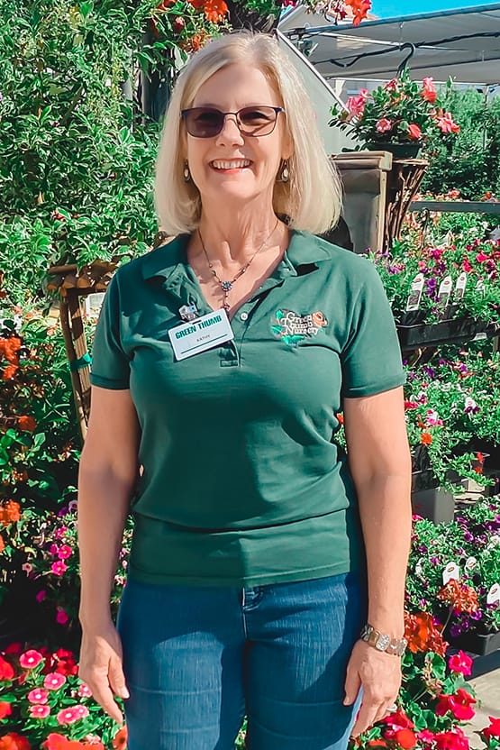 A woman in a green shirt posing near a flower garden at a nursery.