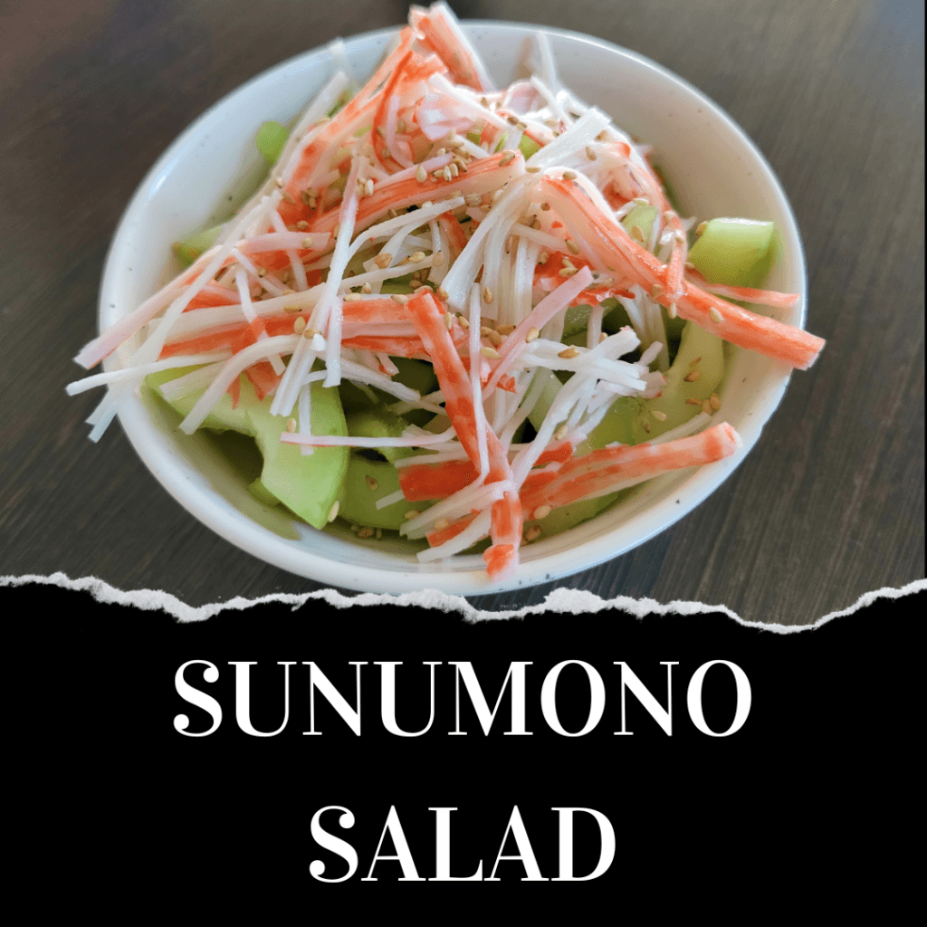 A bowl of Sunomono salad topped with imitation crab sticks, shredded radish, cucumber slices, and sesame seeds on a dark surface.