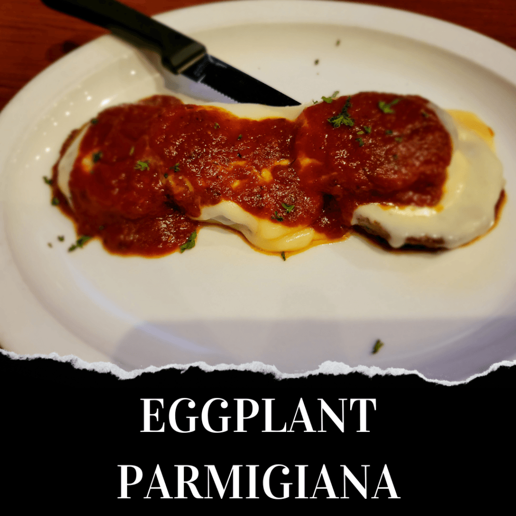A plate of eggplant parmigiana topped with melted cheese and tomato sauce, garnished with herbs, with a black-handled knife beside it.