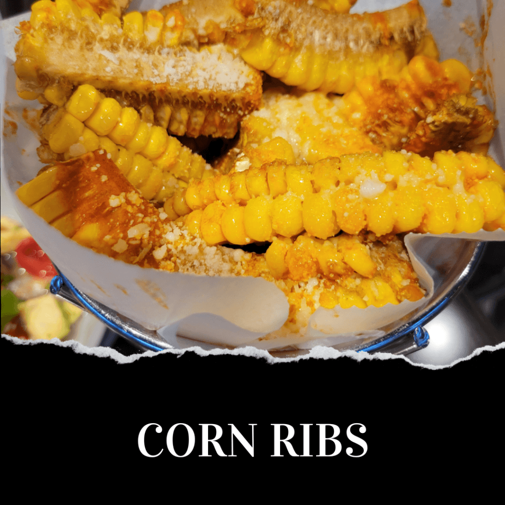 Corn ribs seasoned with spices and cheese are arranged in a metal basket.