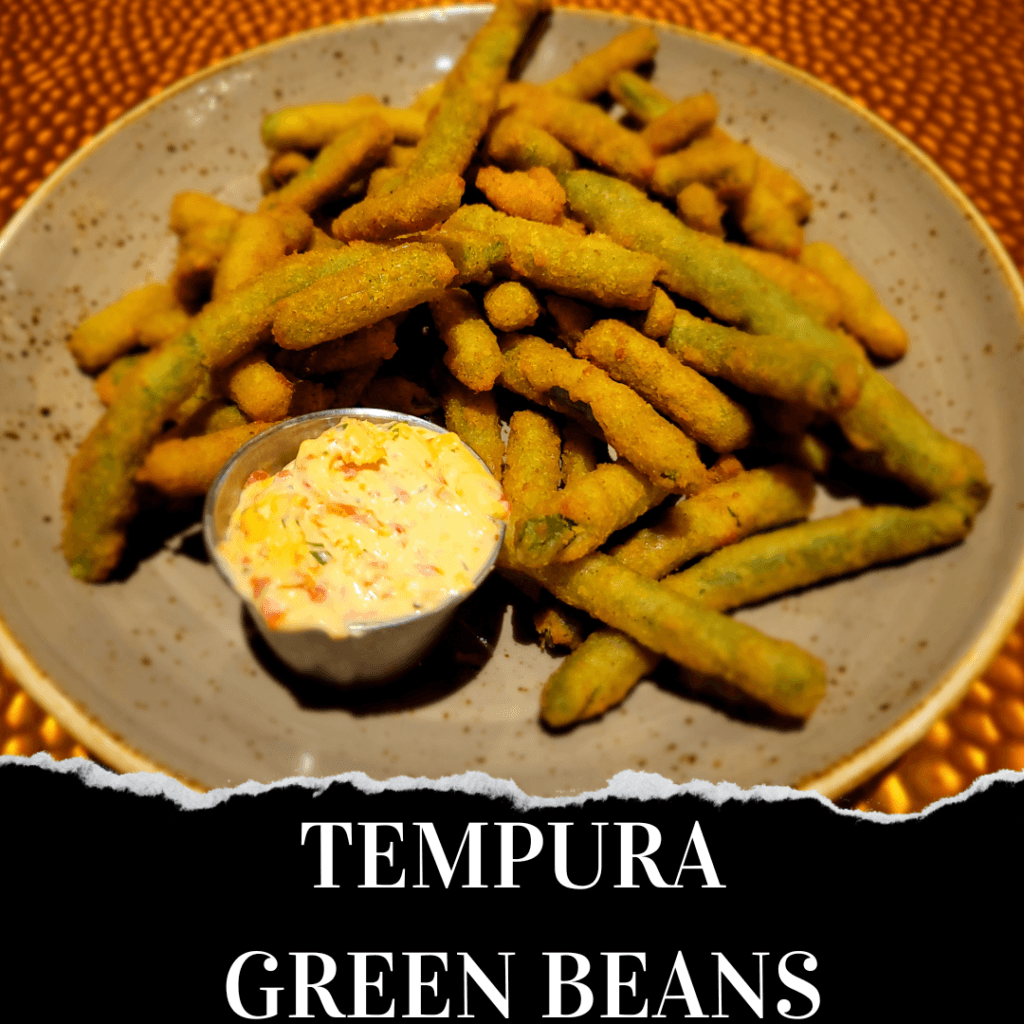 A plate of tempura green beans with a small serving of creamy dipping sauce on the side. Text at the bottom reads "Tempura Green Beans.