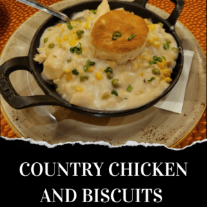 A skillet filled with creamy country chicken and vegetable stew, topped with a biscuit, served on a beige plate.