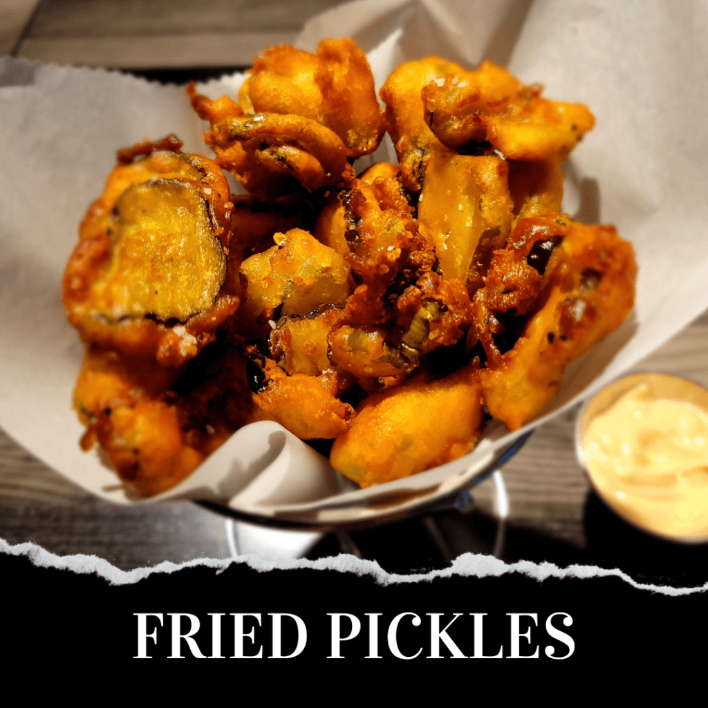 A basket of golden-brown fried pickles on parchment paper, served with a side of dipping sauce. The text "FRIED PICKLES" is displayed at the bottom.