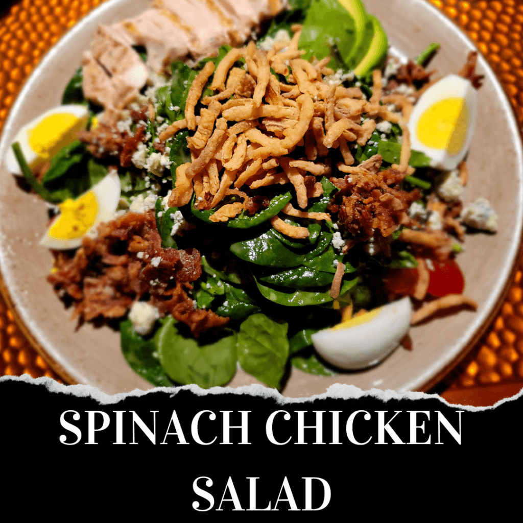 A plate of spinach chicken salad with sliced chicken, boiled eggs, avocado, crispy onions, cheese crumbles, and greens. Text at the bottom reads "Spinach Chicken Salad.