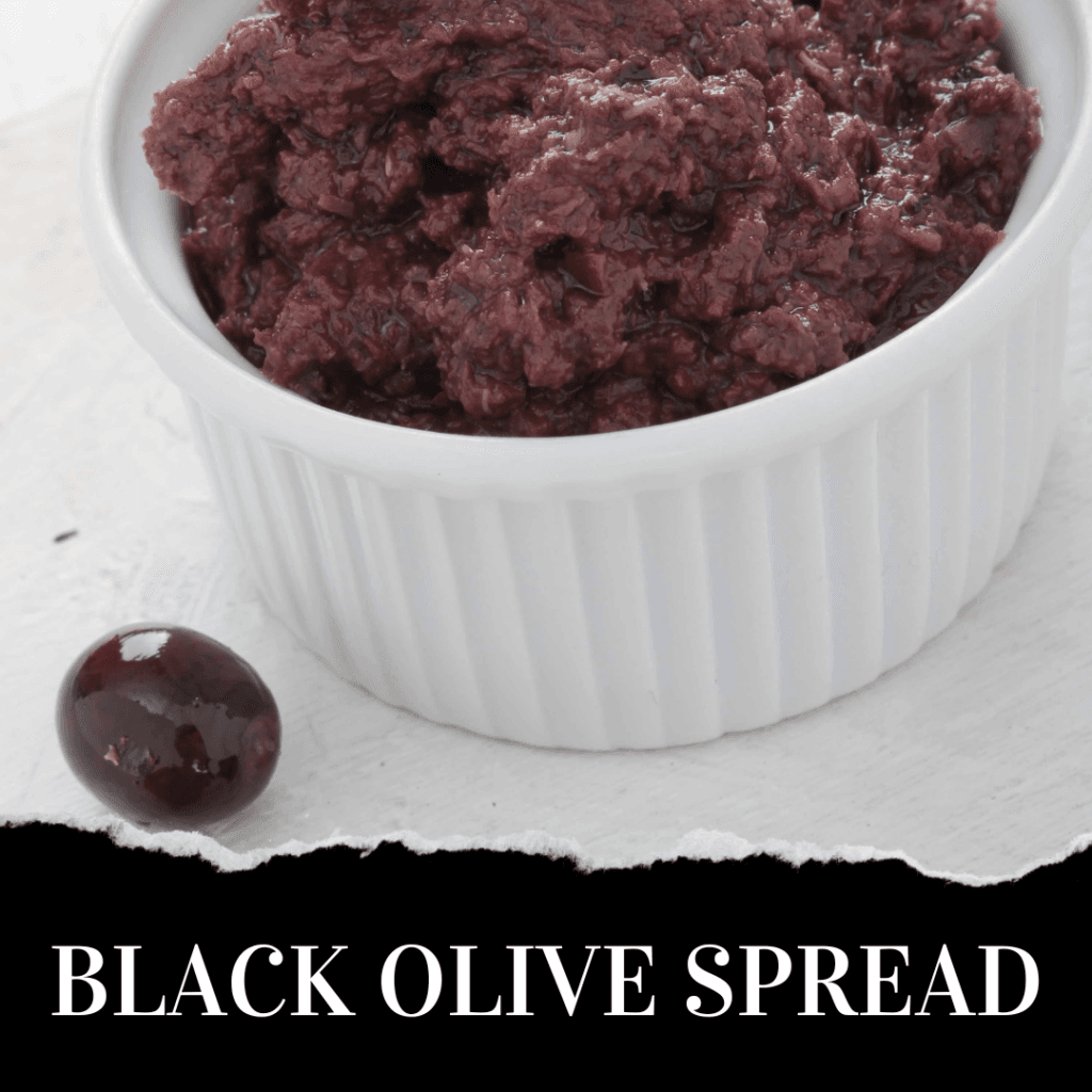 A white ramekin filled with black olive spread sits on a white surface beside a single whole black olive. Text below reads: “BLACK OLIVE SPREAD.”.