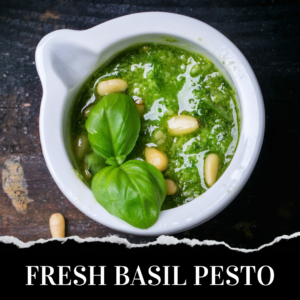 A white mortar filled with green basil pesto, topped with basil leaves and pine nuts, sits on a dark wooden surface. Text at the bottom reads "FRESH BASIL PESTO.