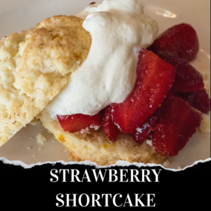 A biscuit-style shortcake topped with sliced strawberries and a dollop of whipped cream on a white plate, labeled "STRAWBERRY SHORTCAKE.