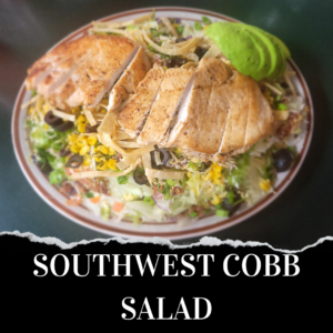 A southwest cobb salad with sliced grilled chicken, corn, black beans, lettuce, tortilla strips, and a scoop of guacamole on a ceramic plate.
