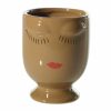 A brown ceramic cup with a closed-eye face design and red lips painted on the front.