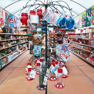 san marcos bird feeders 1 A garden shop aisle displaying bird feeders, colorful glass items, and garden decorations, with shelves on both sides and a canopy above.