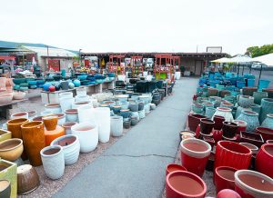 san marcos pottery 2 Outdoor display of various colorful ceramic pots in different shapes and sizes, arranged on a paved area. A building and more garden items are visible in the background.